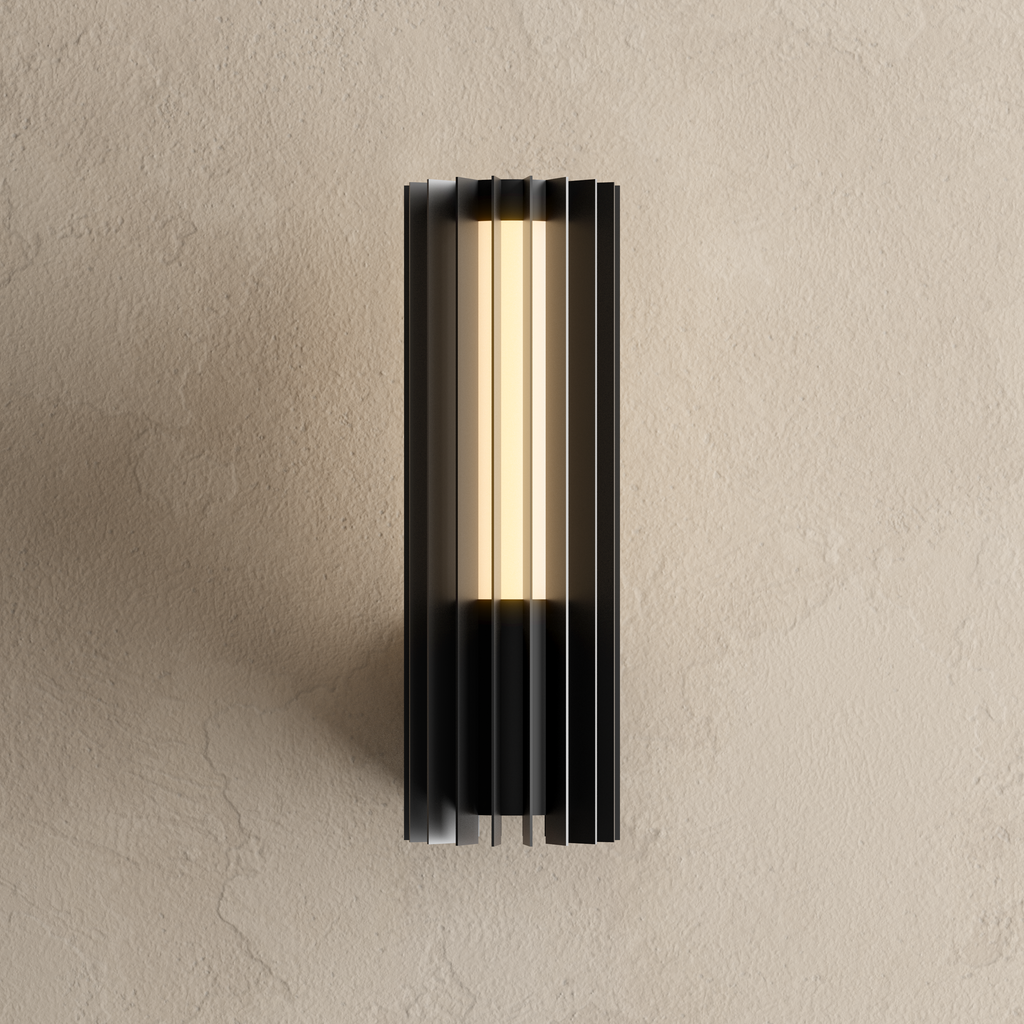 Applique extérieure cylindrique noire à lames d’inox, allumée en blanc chaud sur un mur enduit beige
