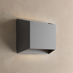 Applique extérieure carrée noire allumée sur un mur beige, lumière diffusée vers le haut et vers le bas