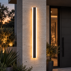 Applique extérieure LED linéaire noire allumée en blanc chaud sur un pilier en pierre, à l'entrée d'une maison le soir