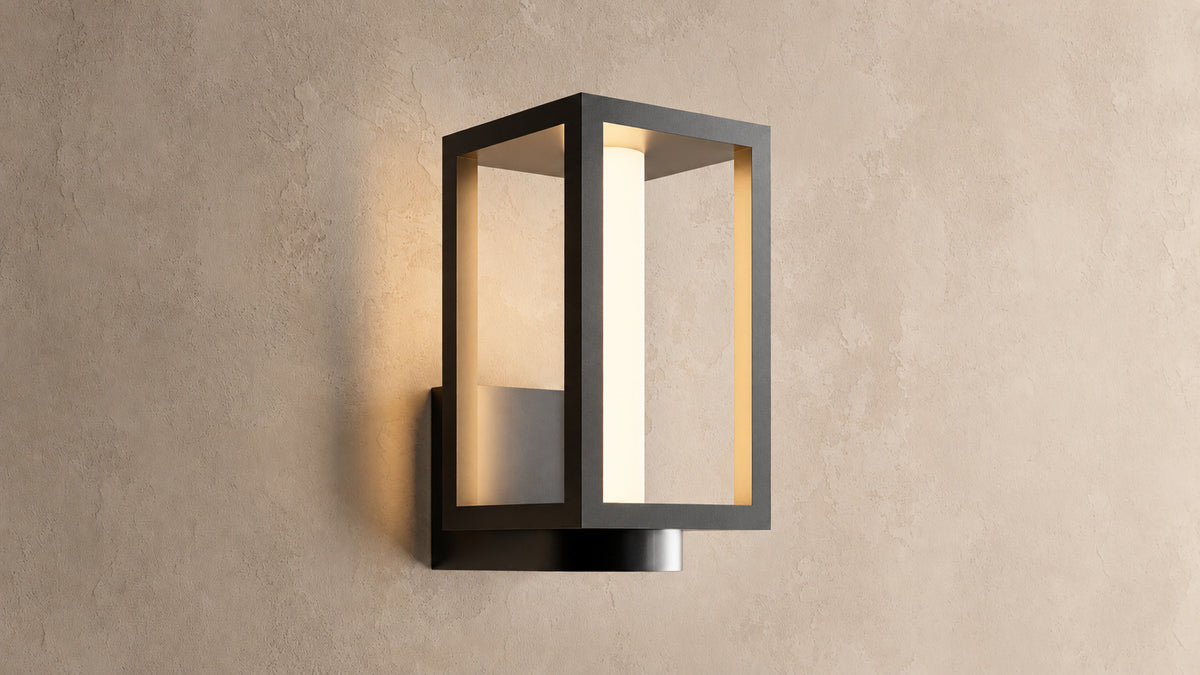 Applique extérieure lanterne noire allumée sur un mur enduit beige, vue de trois quarts