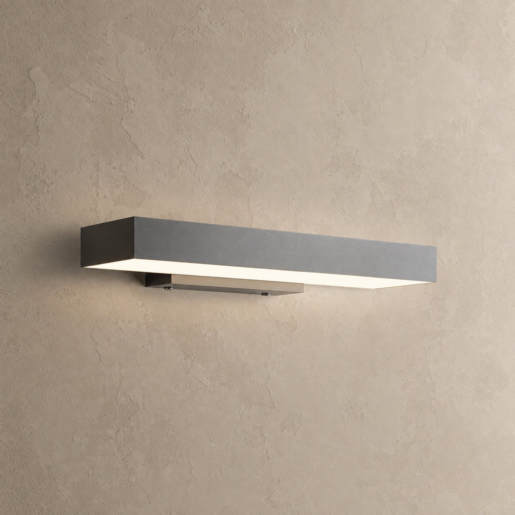 Applique murale extérieure horizontale noire allumée, lumière blanc chaud diffusée vers le bas, sur un mur enduit beige