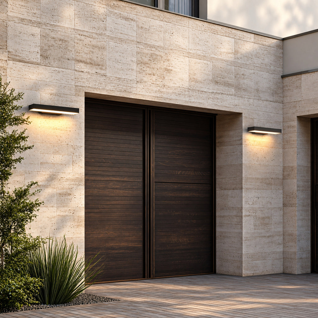 Deux appliques extérieures horizontales noires allumées de part et d’autre d’une porte de garage en bois, façade en pierre claire
