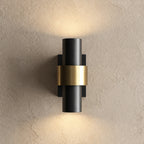 Applique extérieure cylindrique noire à bague dorée, allumée vers le haut et vers le bas sur un mur enduit beige