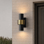 Applique extérieure cylindrique noire et dorée, double halo lumineux sur un mur en brique claire près d’une porte