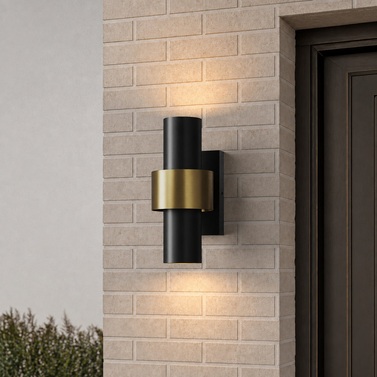Applique extérieure cylindrique noire et dorée, double halo lumineux sur un mur en brique claire près d’une porte