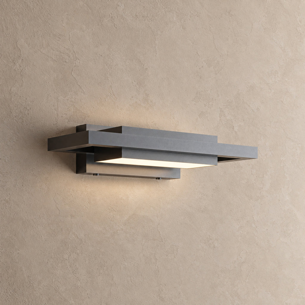 Applique extérieure noire à plans décalés allumée, vue de trois quarts sur un mur beige