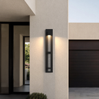 Applique extérieure noire taille Grand, 73 cm, allumée sur la façade d’une maison moderne, près de l’entrée et du garage