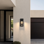Applique extérieure noire taille Petit, 30 cm, allumée sur la façade d’une maison moderne, près de l’entrée et du garage