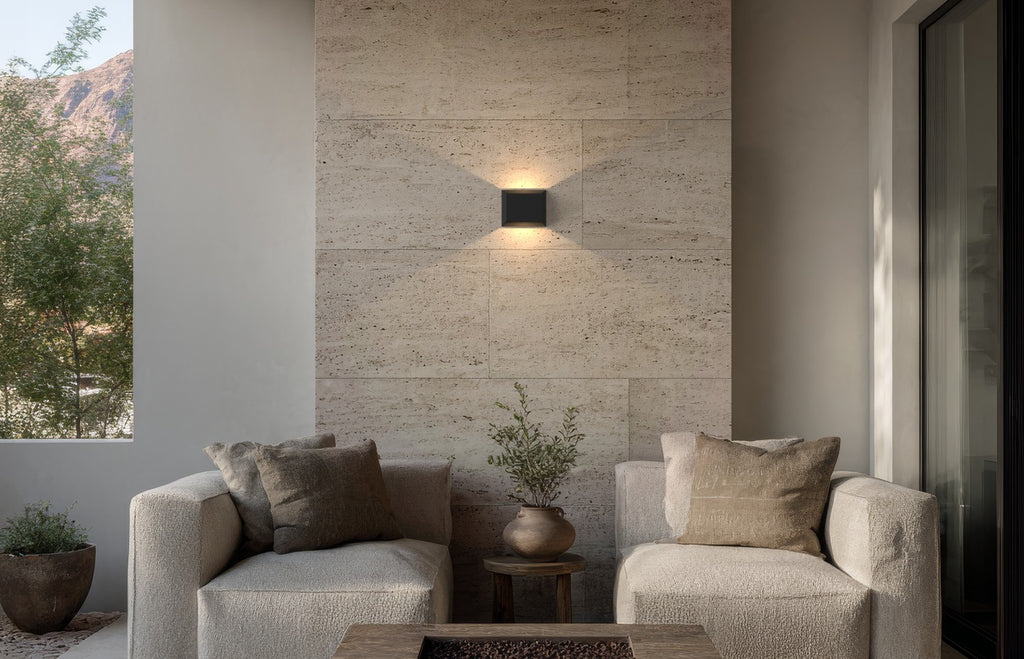 Applique extérieure carrée noire allumée sur un mur en pierre, au-dessus d’un salon de terrasse