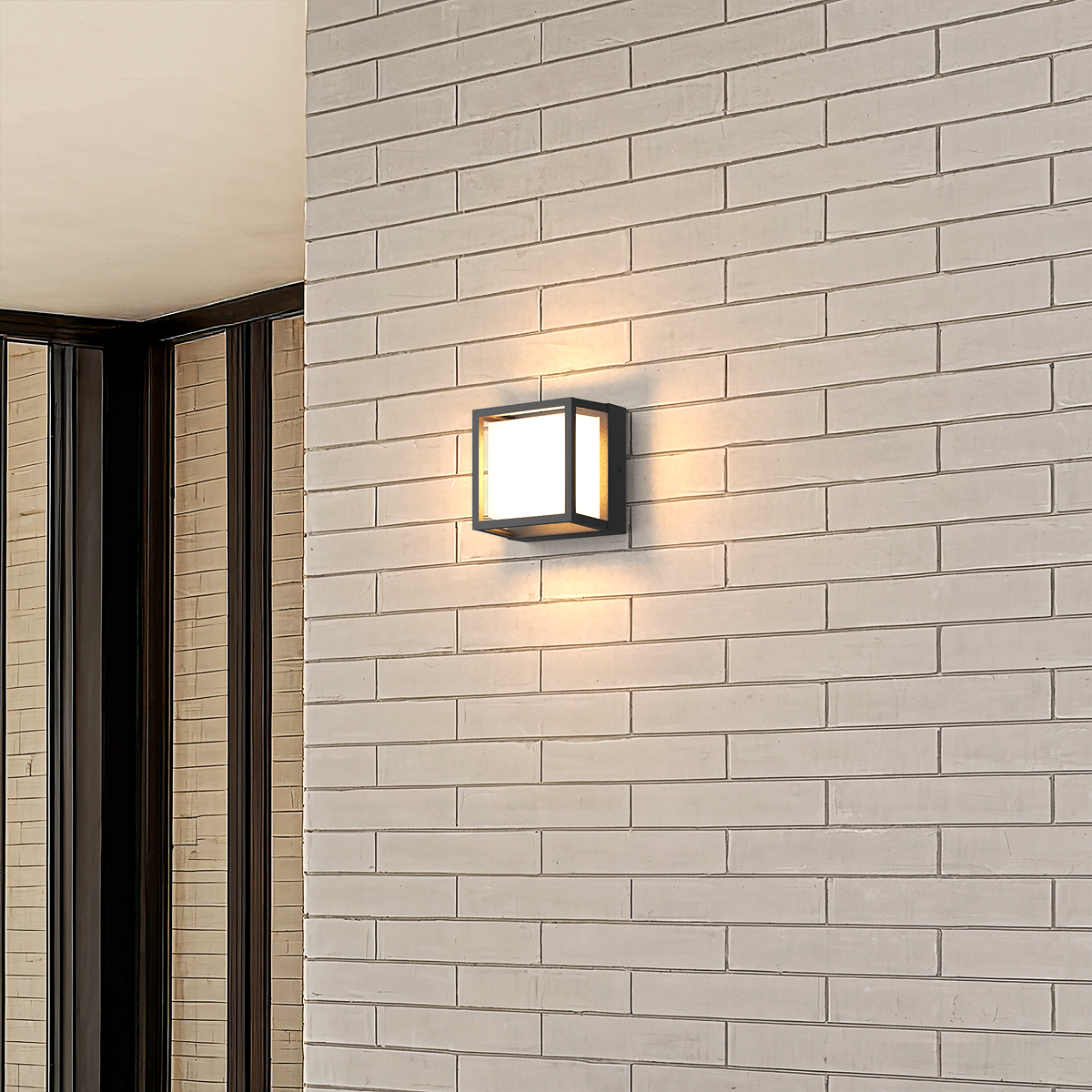 Petit modèle de l’applique extérieure géométrique noire allumé sur un mur en briques blanches