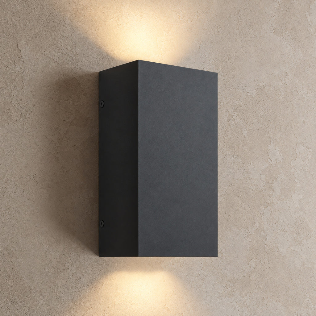 Applique extérieure LED noire rectangulaire allumée, lumière vers le haut et vers le bas sur un mur beige