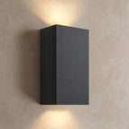Applique extérieure LED noire rectangulaire allumée, lumière vers le haut et vers le bas sur un mur beige