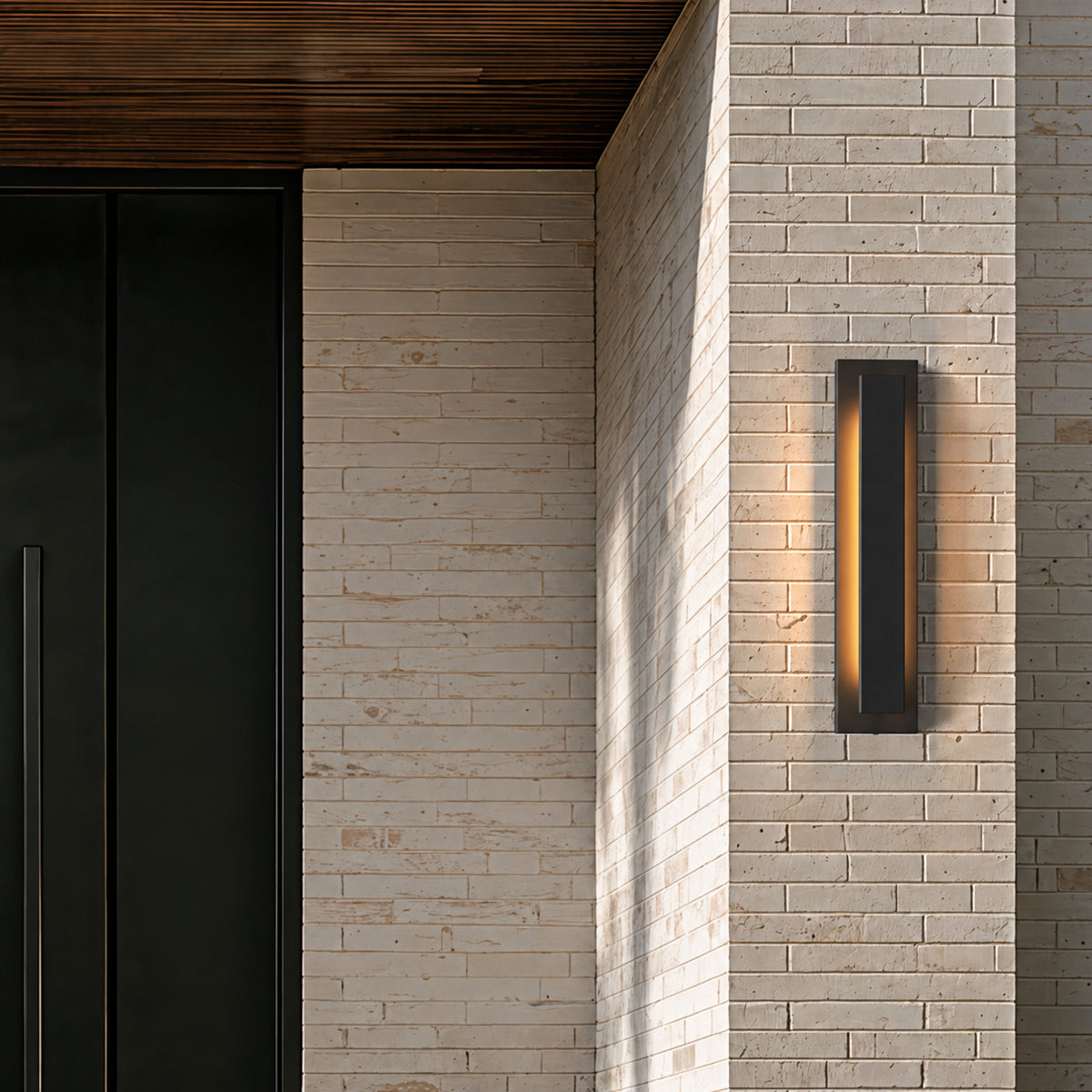 Applique extérieure LED lame verticale noire allumée sur une façade en brique claire, sous un auvent en bois