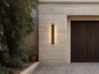Applique extérieure LED verticale allumée sur une façade en pierre claire, près d’une porte de garage en bois