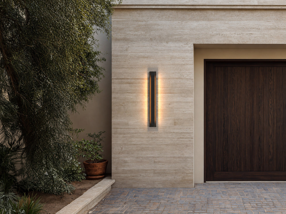 Applique extérieure LED verticale allumée sur une façade en pierre claire, près d’une porte de garage en bois