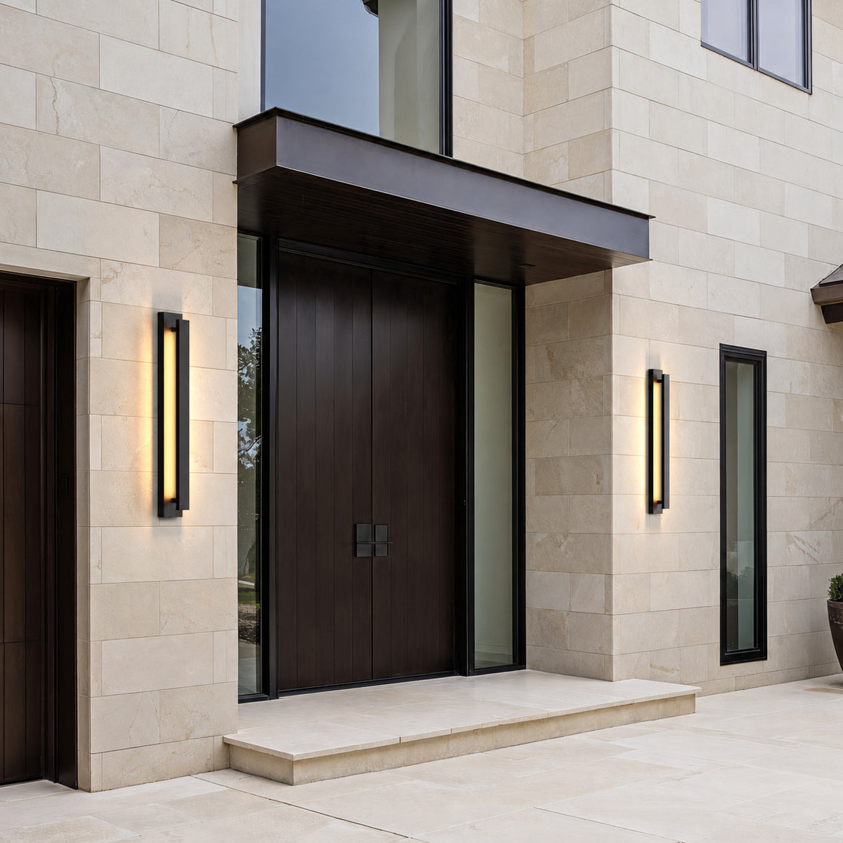 Deux appliques extérieures LED verticales noires encadrant une porte d’entrée sous auvent, façade en pierre claire