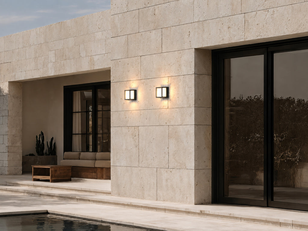 Deux petites appliques noires allumées sur une façade en pierre claire, au bord d’une piscine